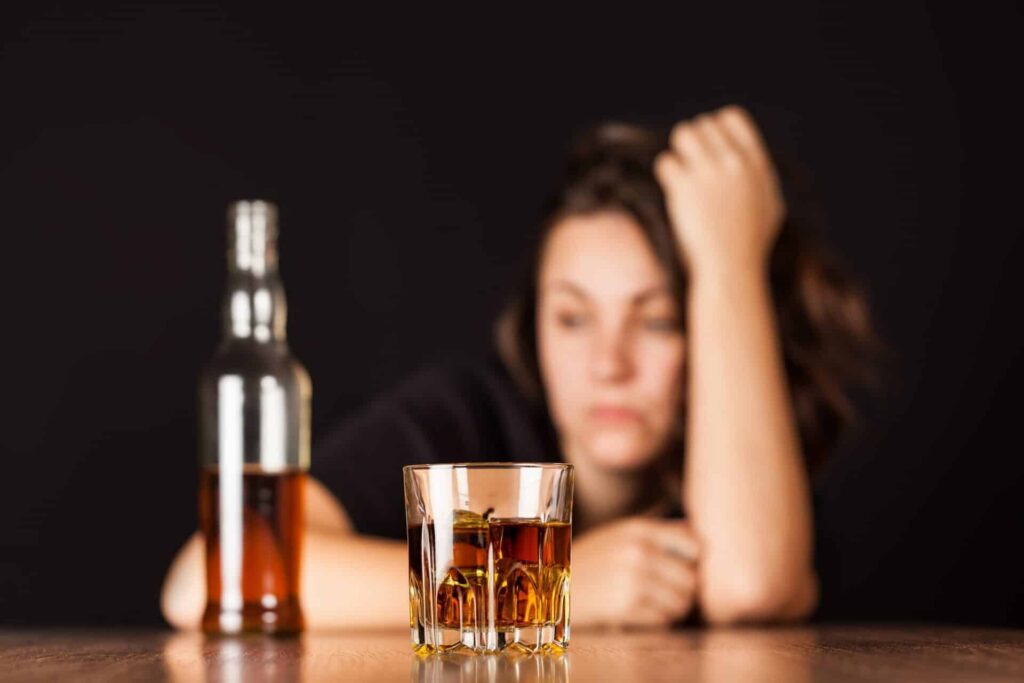 a person looks sad behind a bottle and glass of liquor