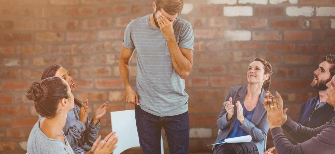 a person stands crying in a therapy group while others applaud