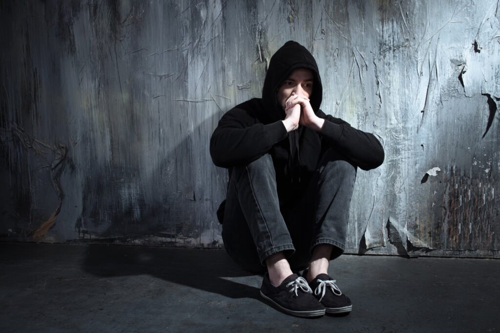 a person struggling with substance abuse sits in sadness in a dark room