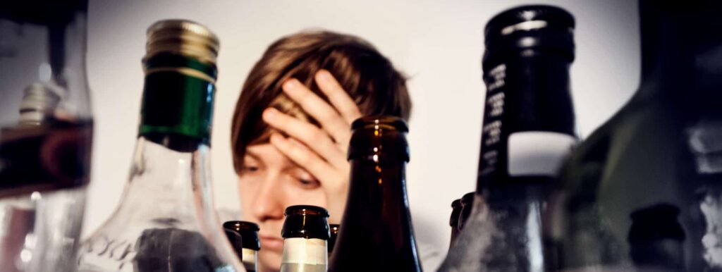 a person looks depressed behind empty alcohol bottles