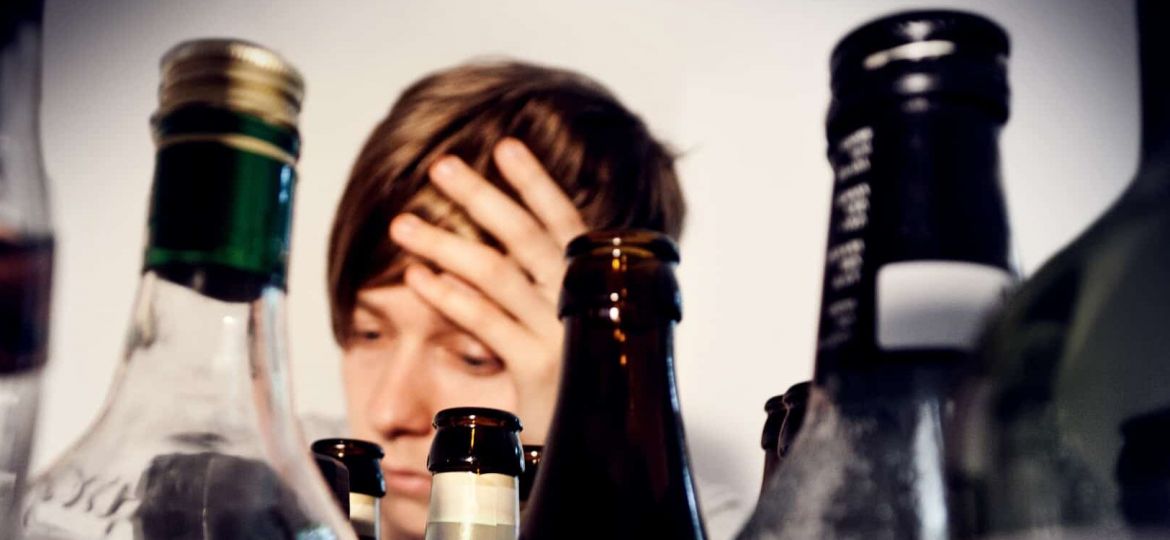 a person looks depressed behind empty alcohol bottles