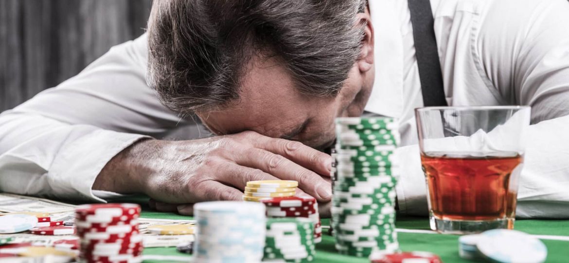 a person puts their head on a poker table behind chips and a glass of liquor