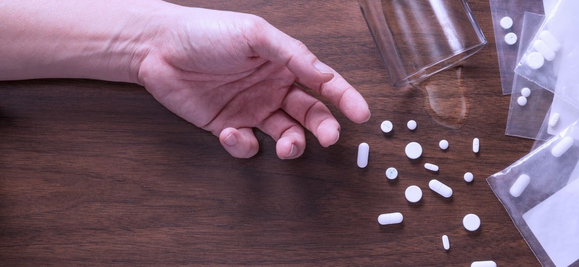 a hand of someone passed out next to scattered pills