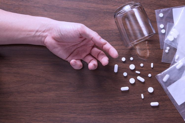 a hand of someone passed out next to scattered pills