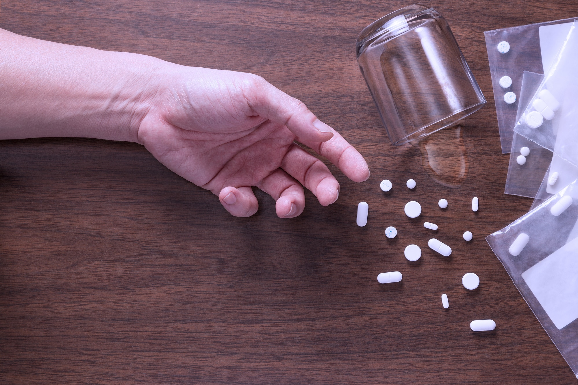 a hand of someone passed out next to scattered pills