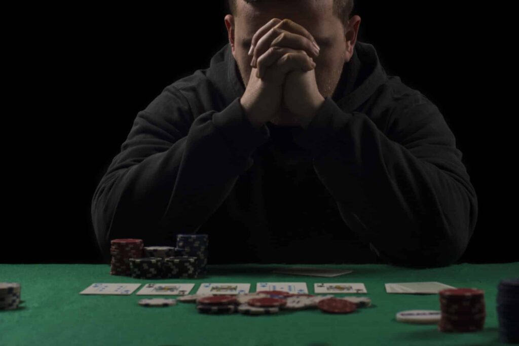 a person looks hopeless while holding their hands to their face behind a poker table