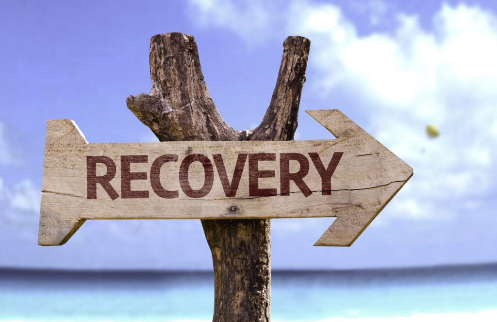 an arrow sign on a beach that says "recovery"