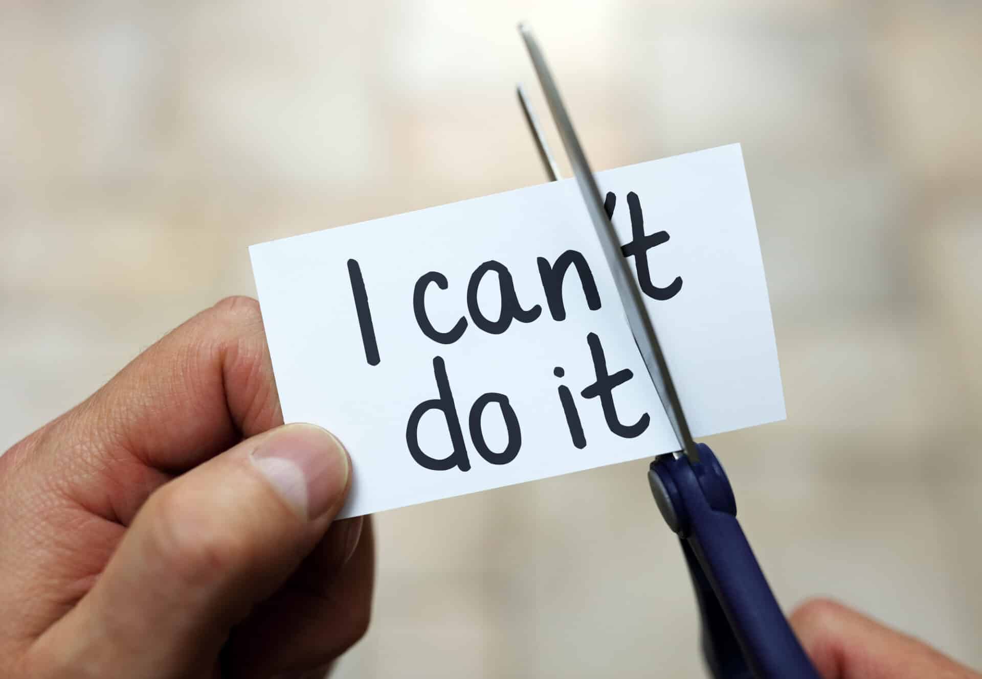 a person cuts the "'t" off of a card reading "I can't do it"