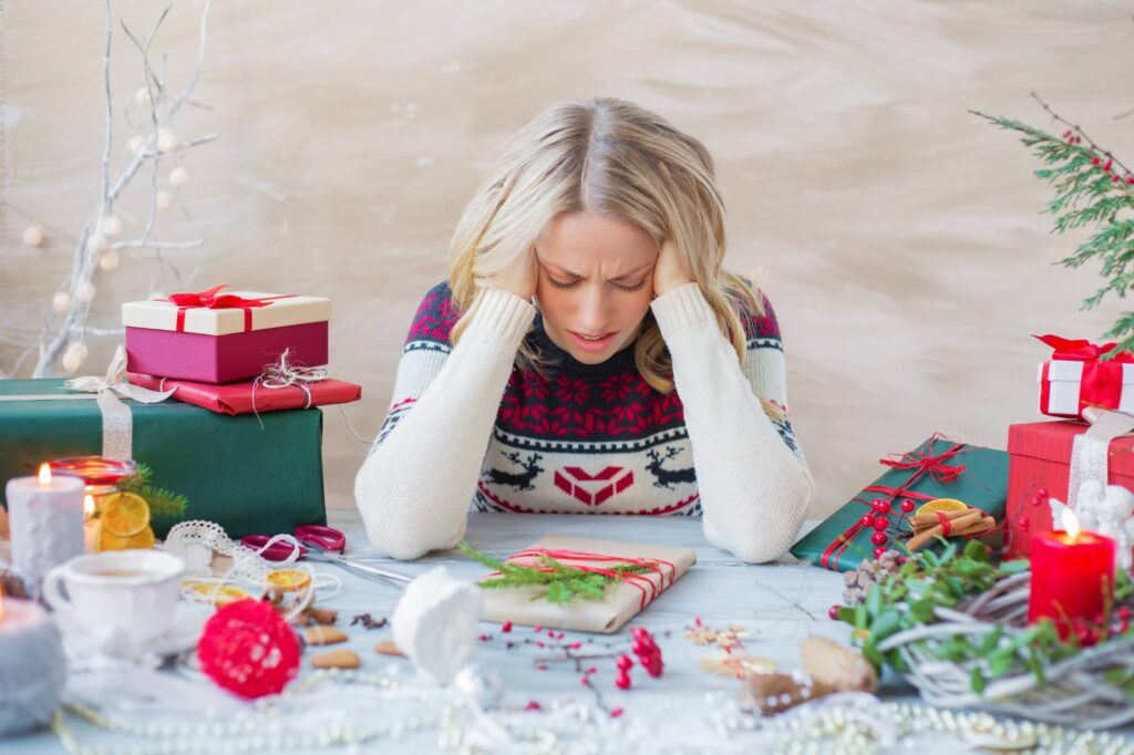 a person holds their head in agony while looking at a wrapped gift on a table during christmas