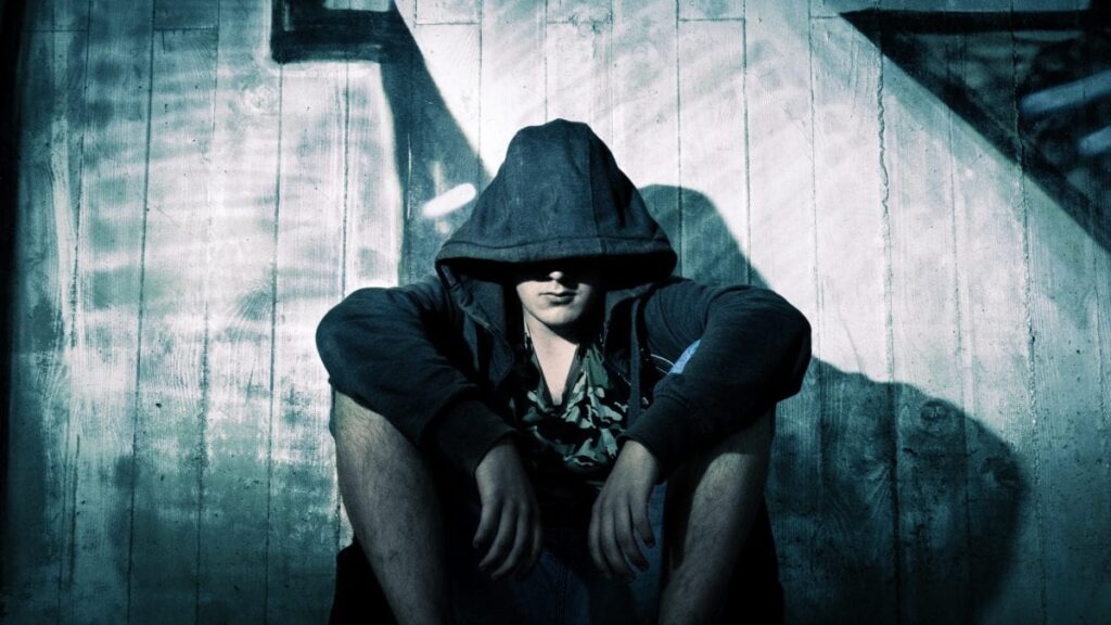 a person with a hood on sits sadly on a floor