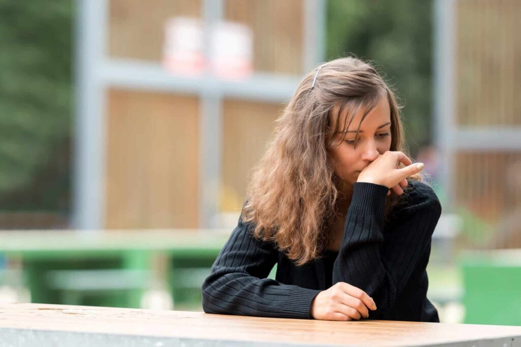 a person sitting at a bench outdoors looks sad