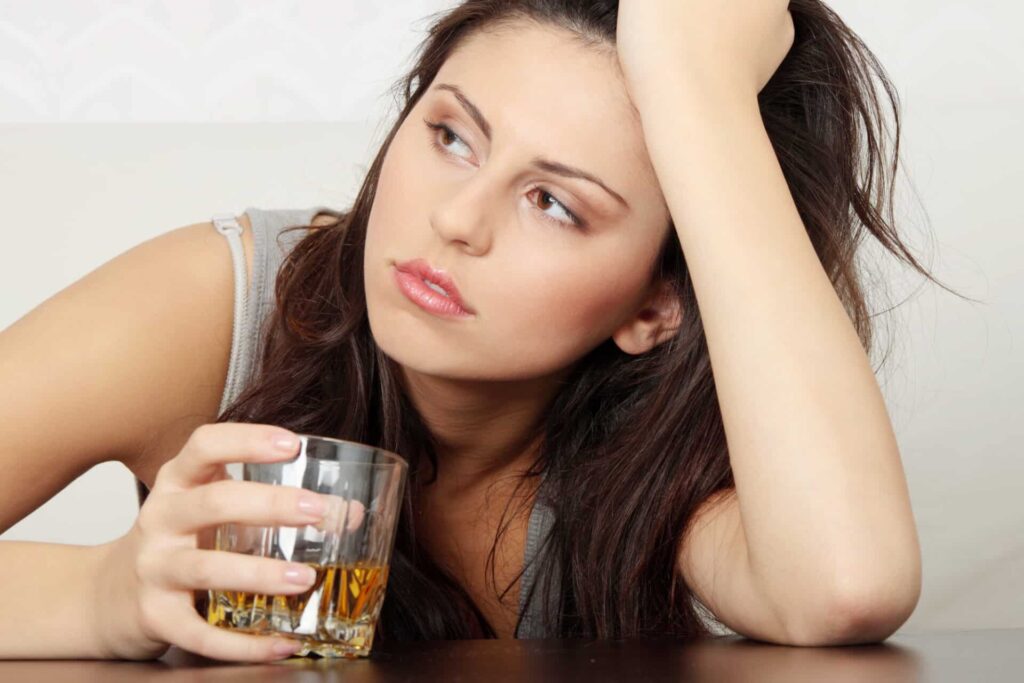 a person holds a glass of liquor while looking anxious and defeated