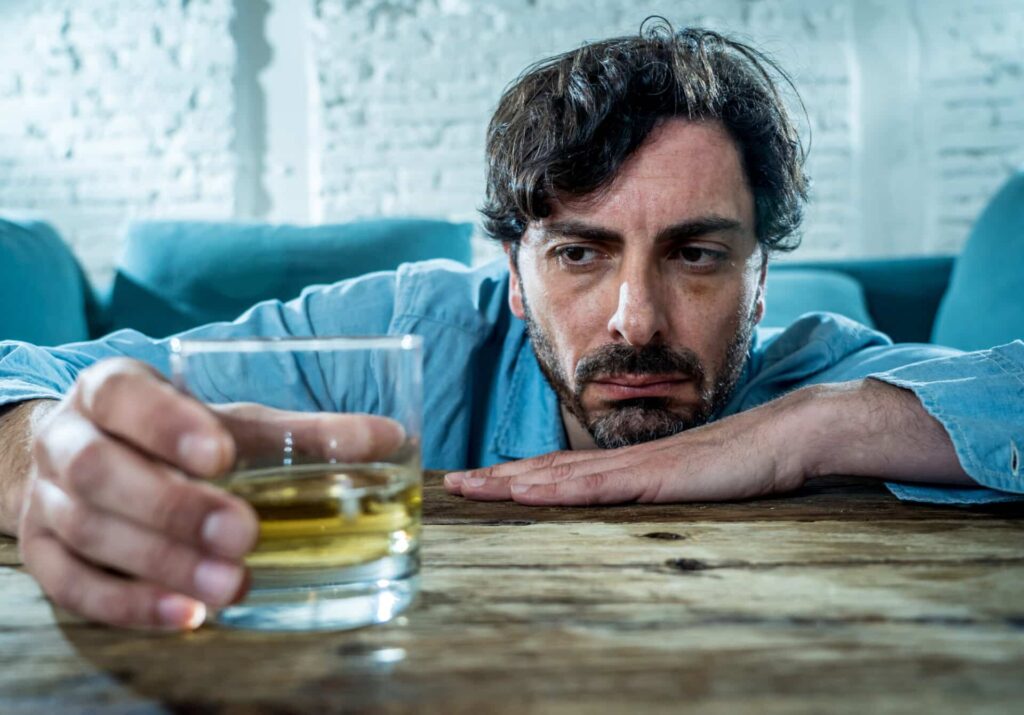 a person looks dejectedly toward a glass of liquor