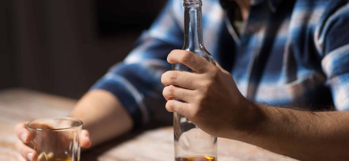 a person holds a glass and bottle of brown liquor