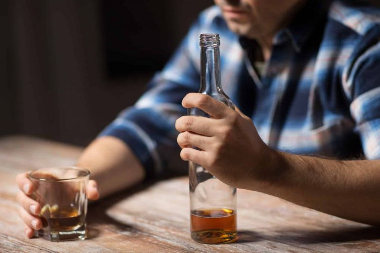 a person holds a glass and bottle of brown liquor
