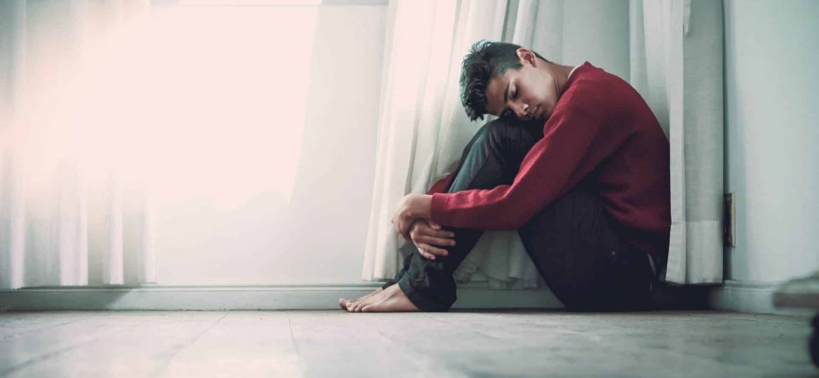 a person holds their head to their knees sitting on a floor