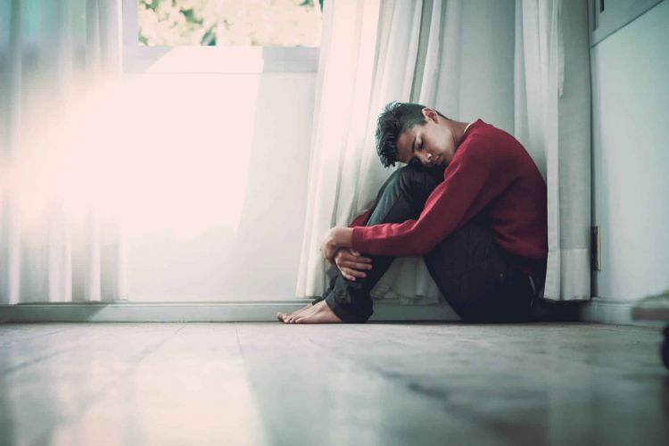 a person holds their head to their knees sitting on a floor