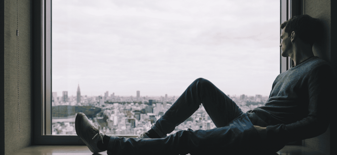 a person sadly looks out a window while sitting in a sill