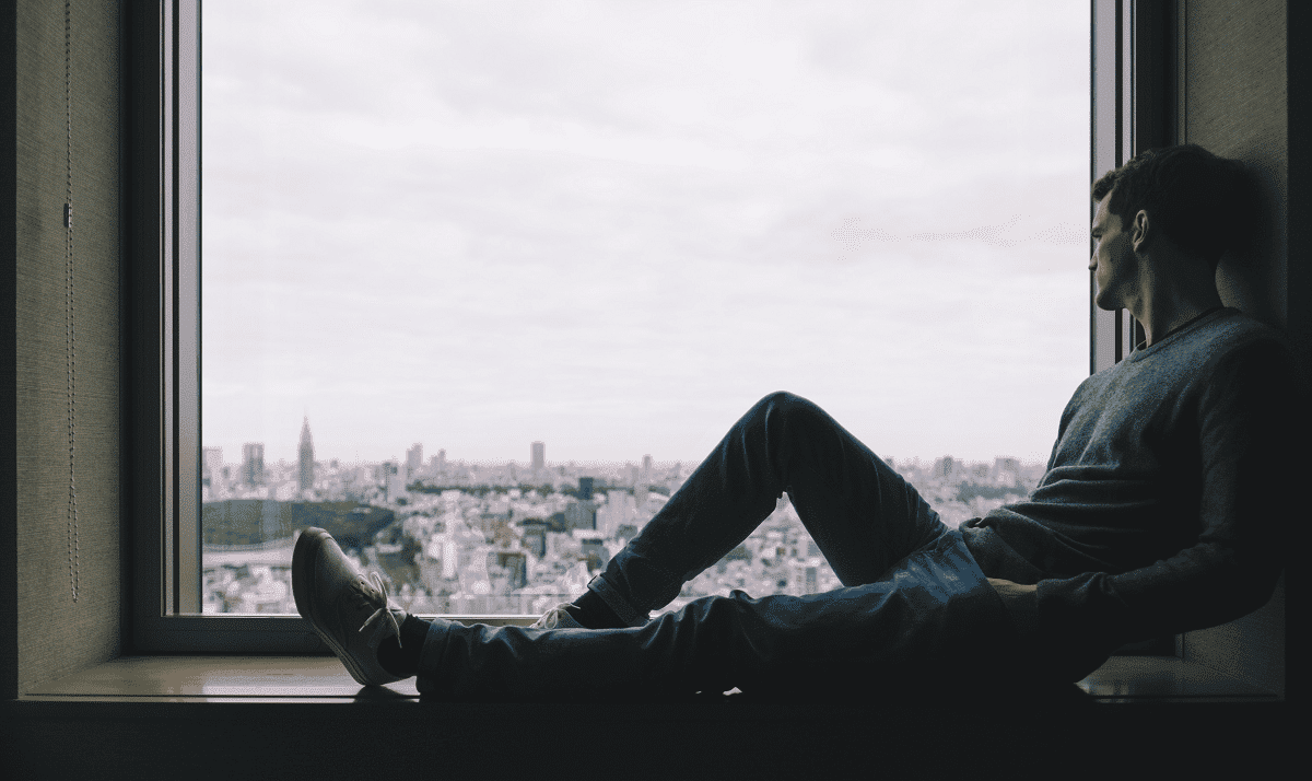 a person sadly looks out a window while sitting in a sill