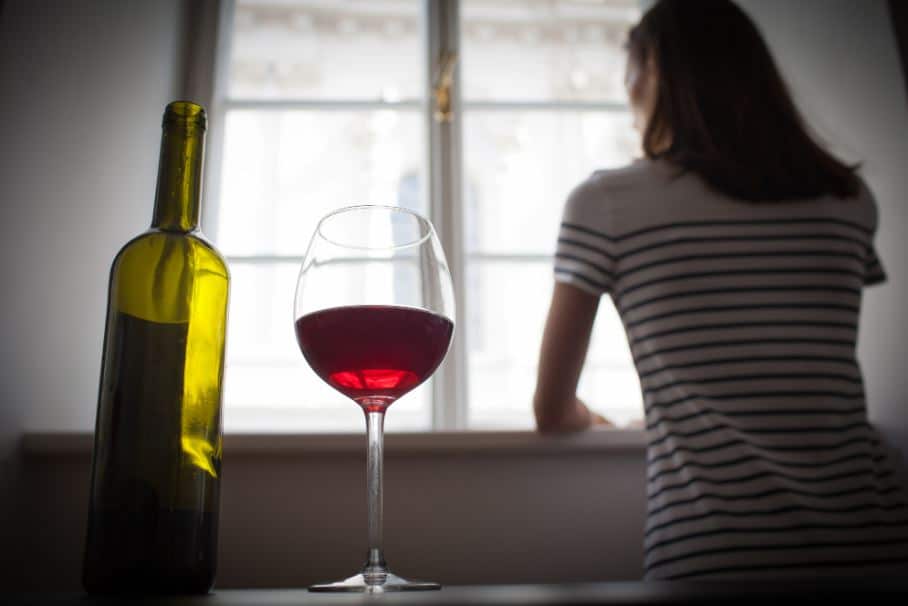 a person looks out of a window behind a glass of wine and a bottle