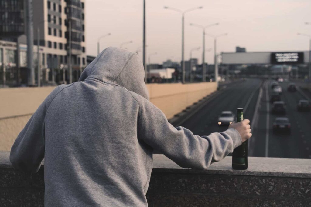 a person on an overpass holds a beer bottle