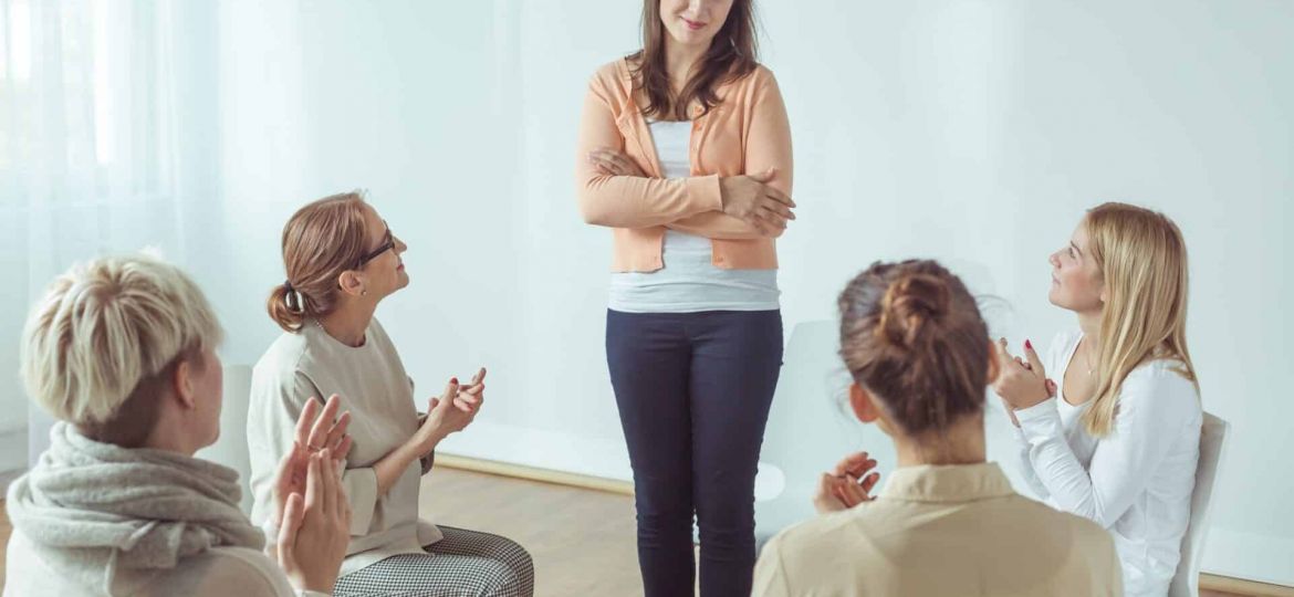 a person stands and shares as a therapy group applauds