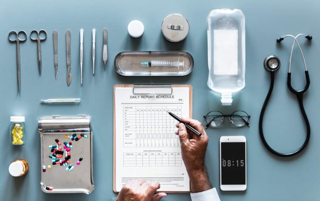 a doctor holds a pen toward a "daily report schedule" that is arranged near tools and medications