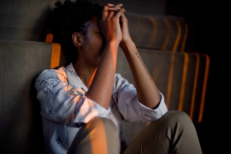person sits with their hands to their face leaning on a couch