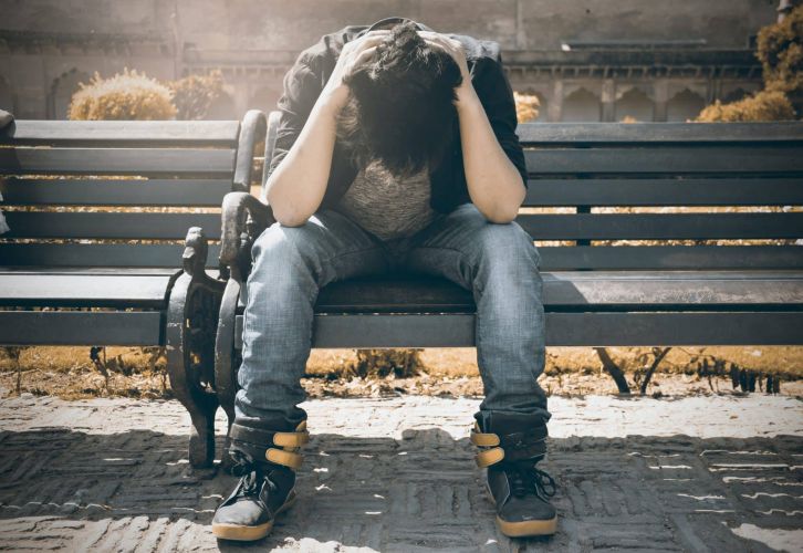 a person holds their neck in agony while hunched on a bench