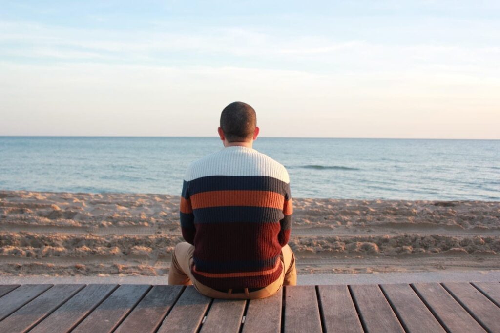 a person sits on a beach boardwalk looking at the ocean