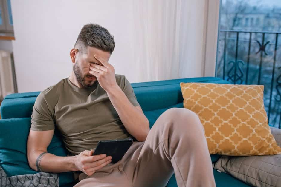 a person pinches their eyes while holding a tablet on a couch