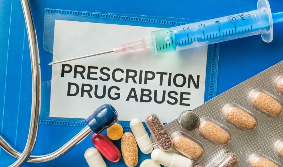 a needle, pills, and a stethoscope on top of a card titled "prescription drug abuse"
