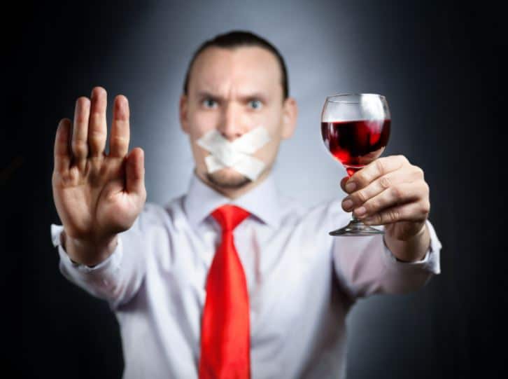 a person with a duct taped mouth holds up a wine glass and palm signalling "stop"