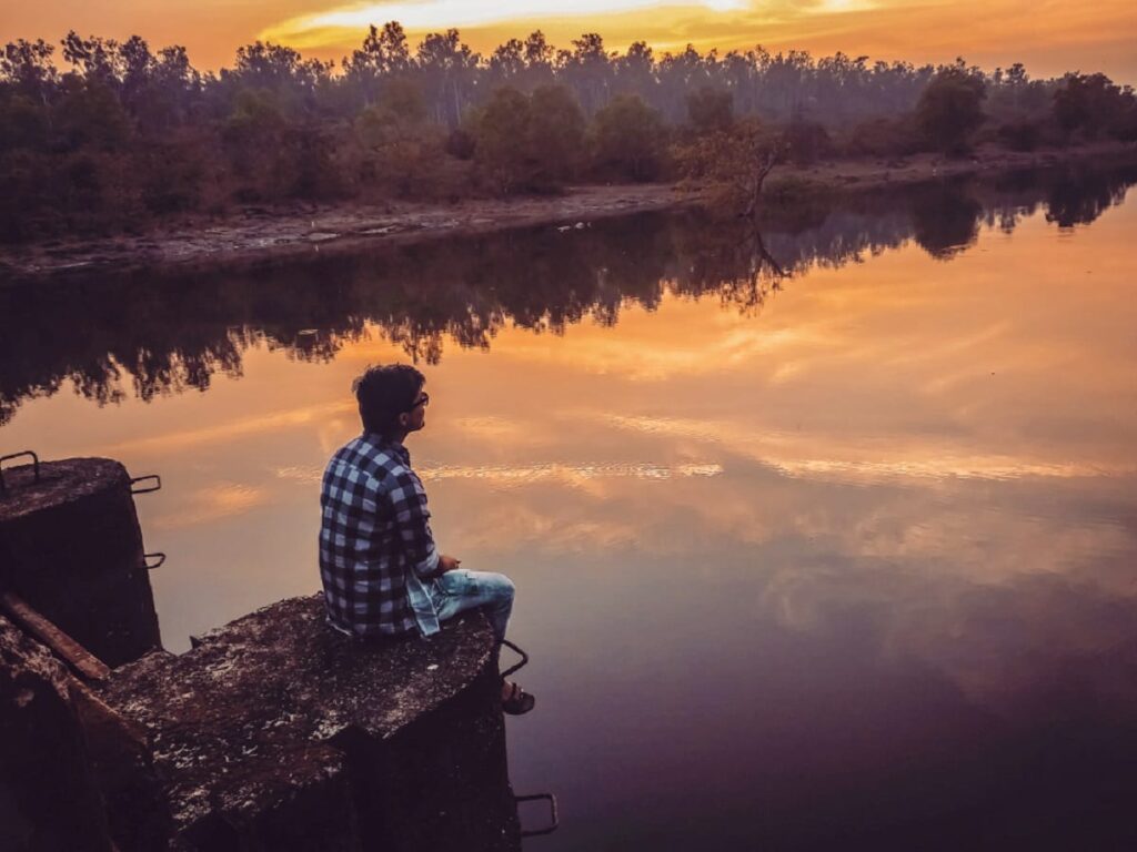 a person sits near a lake at sunset