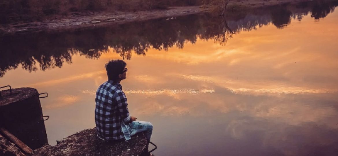 a person sits near a lake at sunset