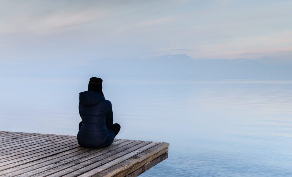 a person sits on a pier on a foggy mountain lake