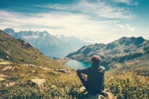 a person meditates overlooking a mountain lake