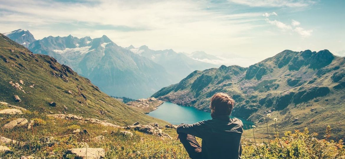 a person meditates overlooking a mountain lake