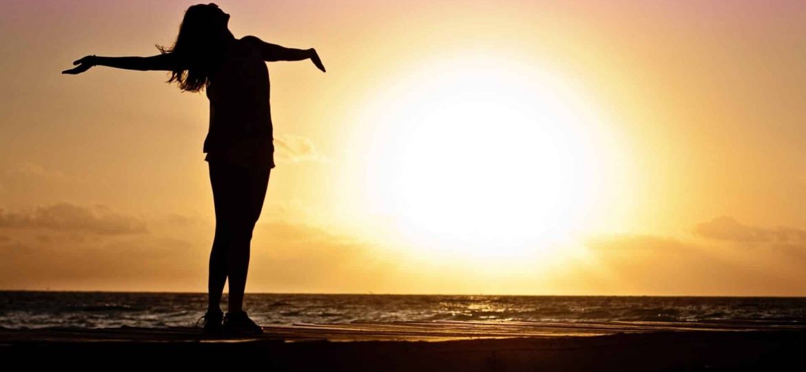 a person celebrates by stretching on a pier at sunset