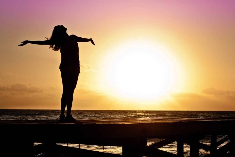 a person celebrates by stretching on a pier at sunset