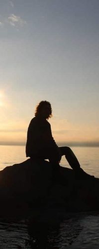 a person sits on a rock in the ocean off the beach