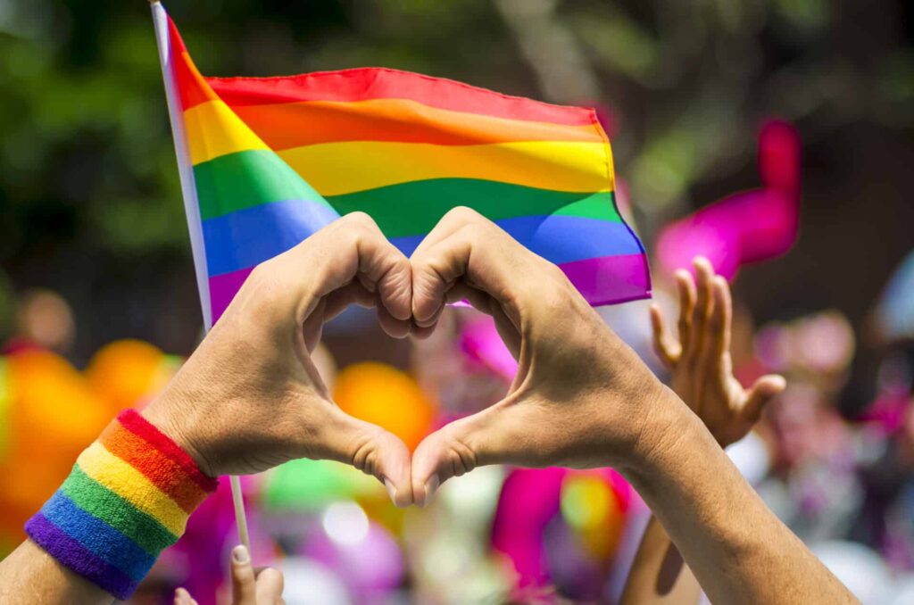 a pride flag with hands holding a heart up