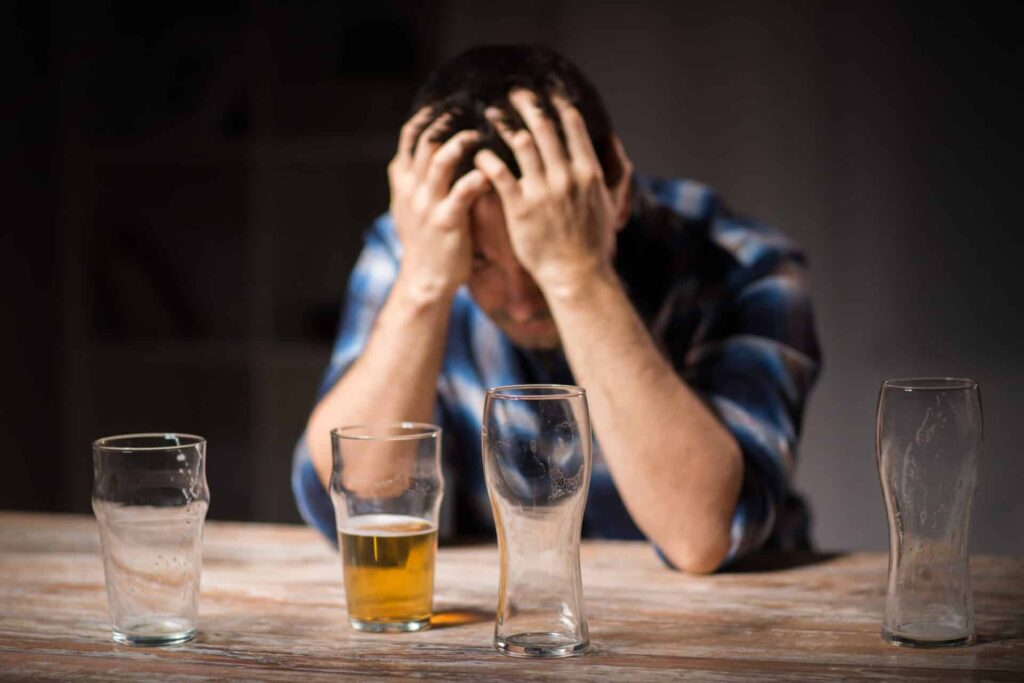 a person holds their head anxiously behind empty beer glasses