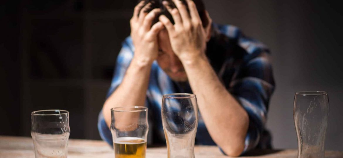a person holds their head anxiously behind empty beer glasses