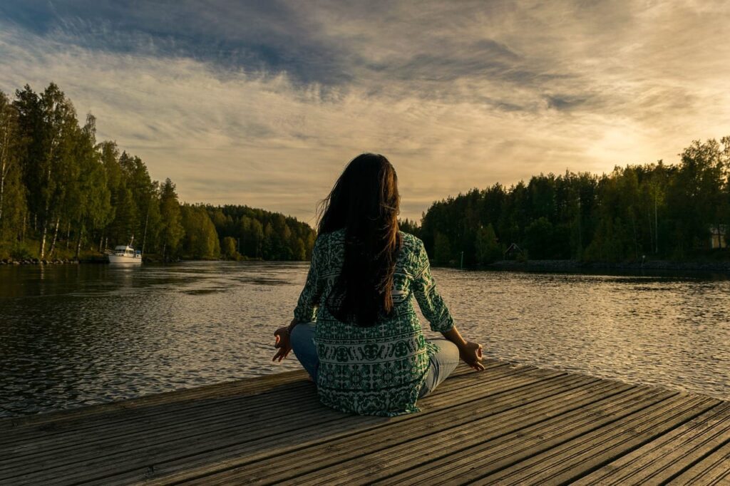 a person meditates on a lake dock