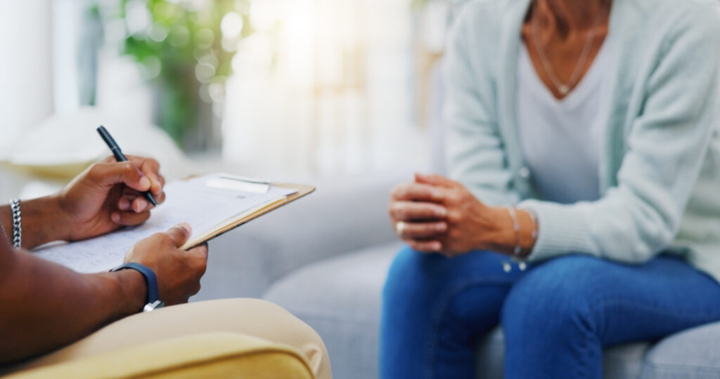 Woman, hands on consulting a therapist writing on clipboard notes for healthcare service of cancer therapy. Closeup, psychology help or patient talking in counseling with paperwork report documents.