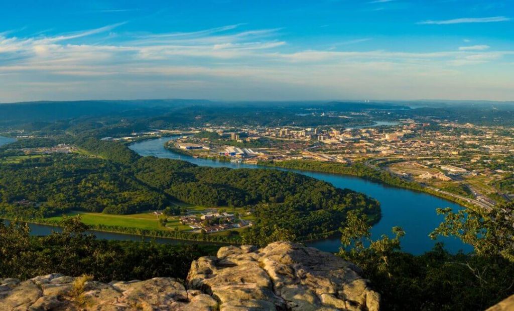 Aerial view of Chattanooga, Tennessee, showcasing the winding Tennessee River surrounded by lush green forests and the urban skyline under a clear blue sky.