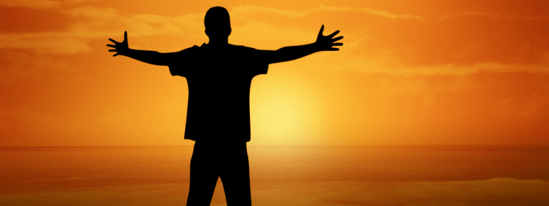 A person stands with their arms outstretched against a sunset.