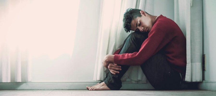 young man sits on the floors with his knees to his chest as he struggles with mental health issues